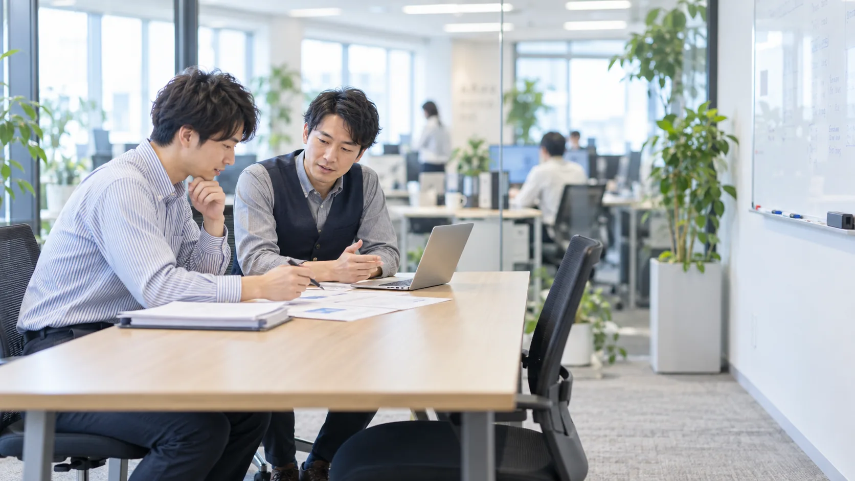 20代後半の日本人男性が小会議室での打ち合わせをしている場面