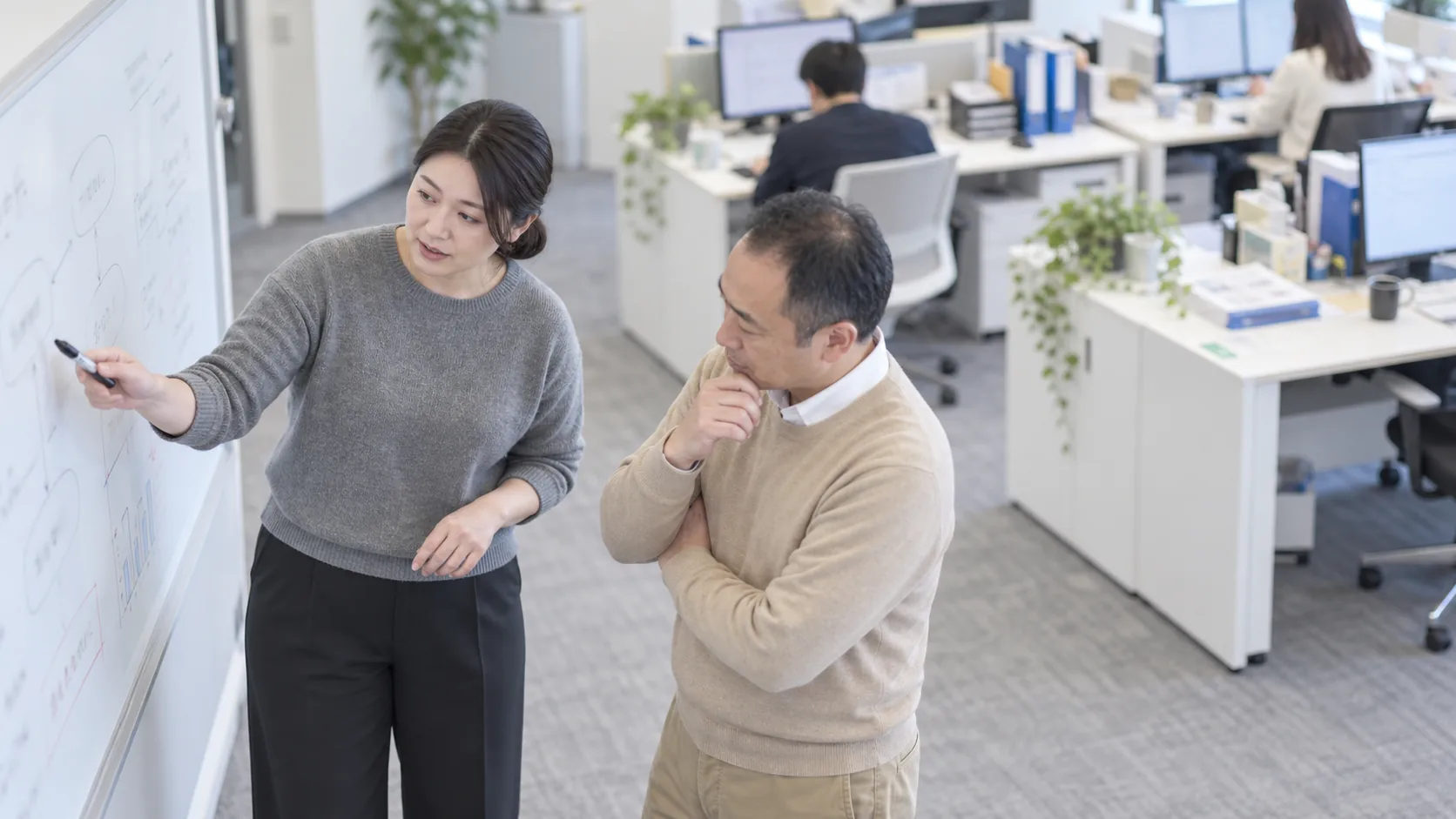 30代後半の日本人女性がホワイトボードでの説明をしている場面