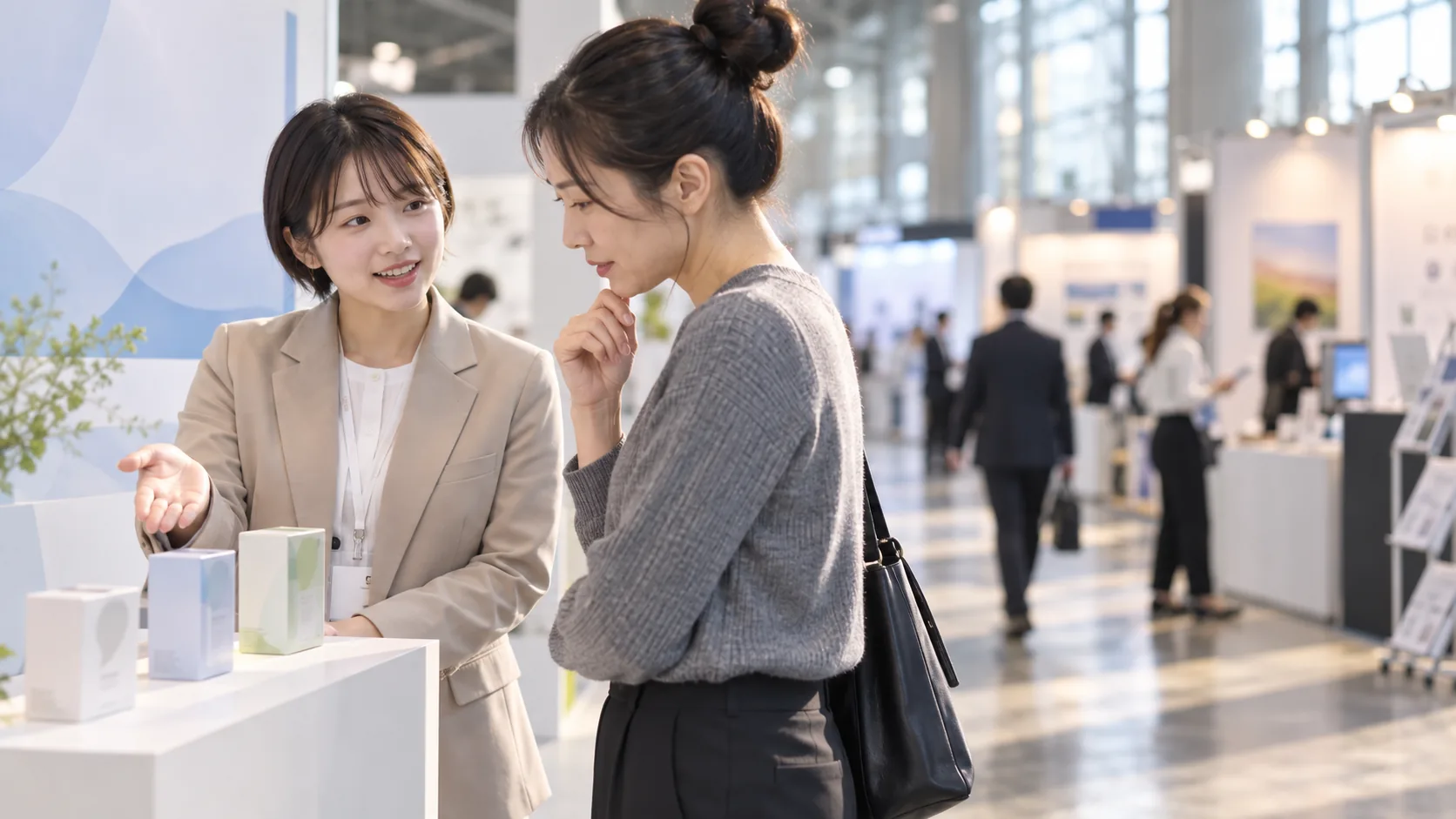 20代前半の日本人女性が展示会のブースでの説明をしている場面
