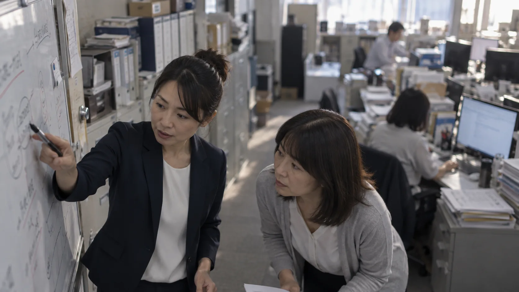 40代前半の日本人女性がホワイトボードでの説明をしている場面