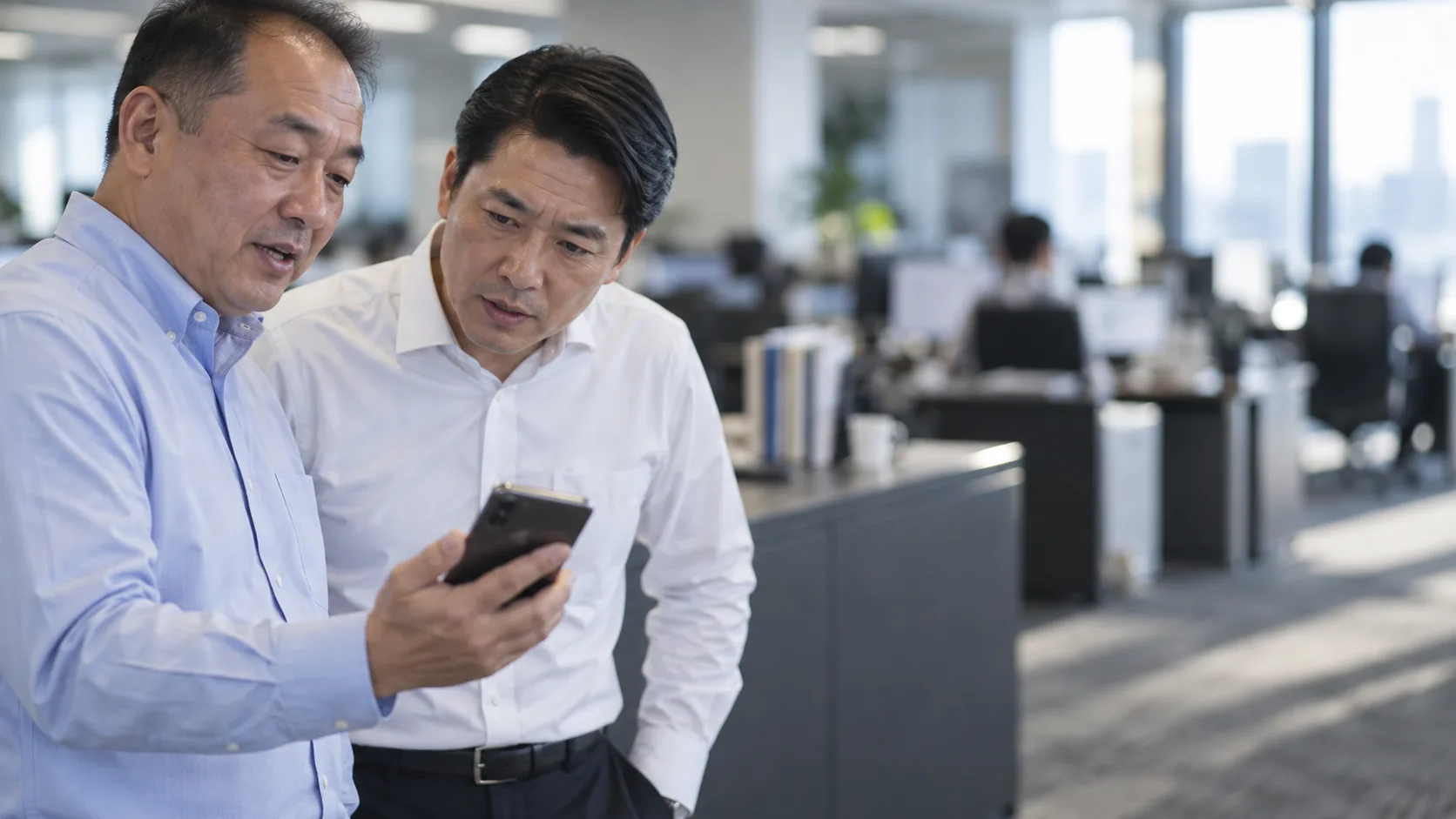 50代前半の日本人男性がスマートフォンの画面提示をしている場面