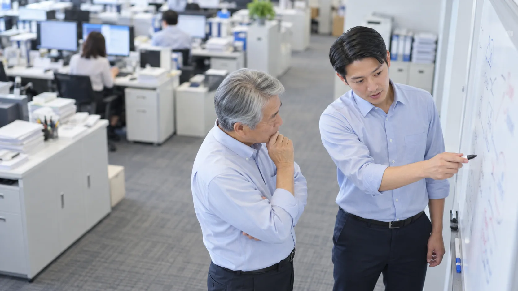 20代後半の日本人男性がホワイトボードでの説明をしている場面