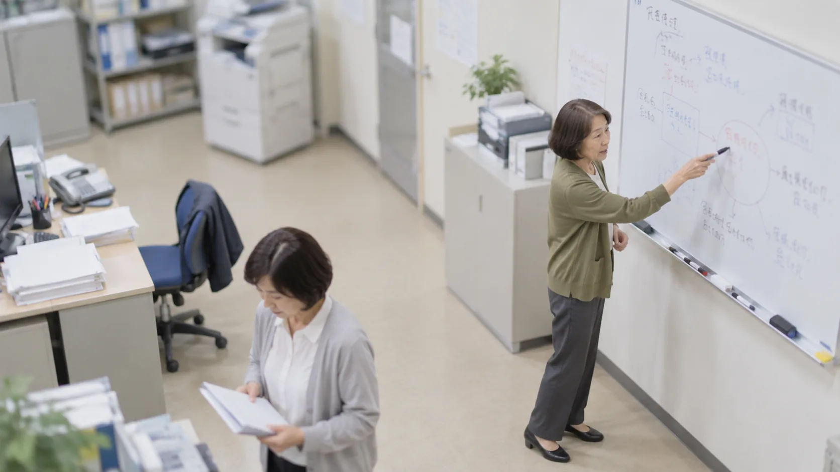 60代前半の日本人女性がホワイトボードでの説明をしている場面