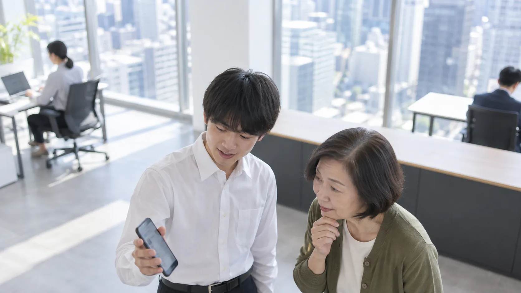 20代前半の日本人男性がスマートフォンの画面提示をしている場面
