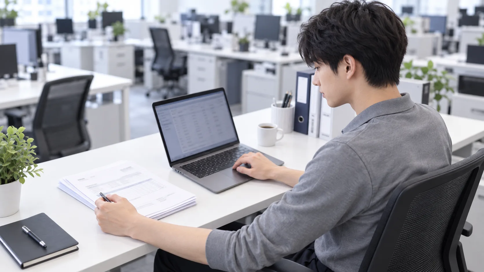 20代前半の日本人男性が自席での書類確認をしている場面