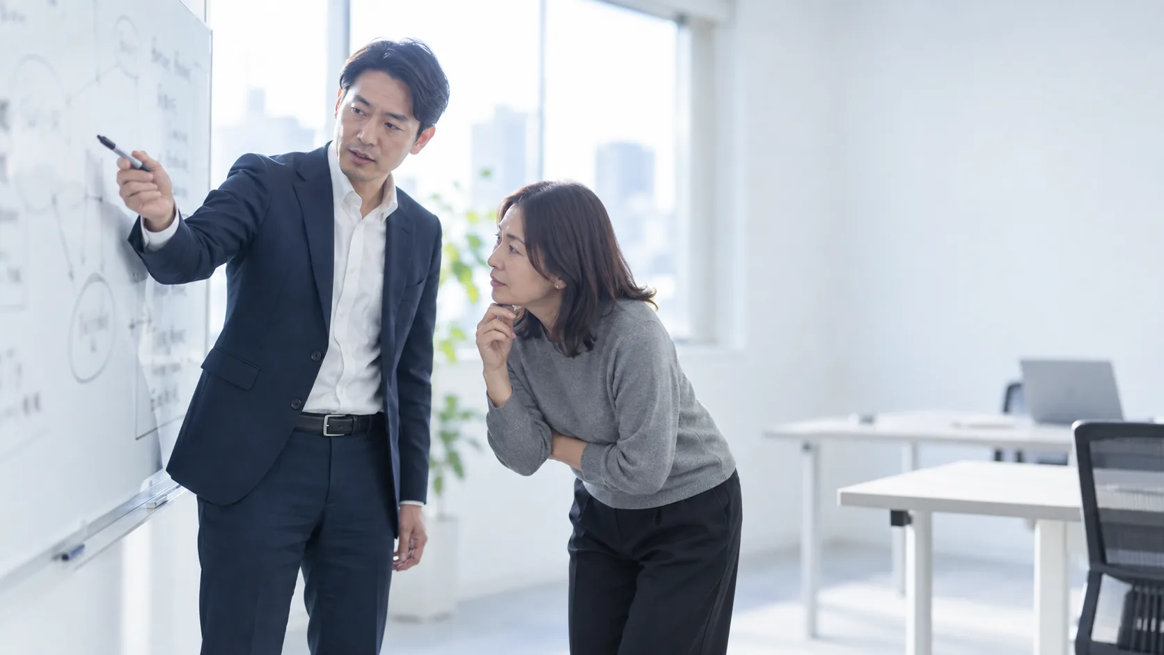 30代後半の日本人男性がホワイトボードでの説明をしている場面