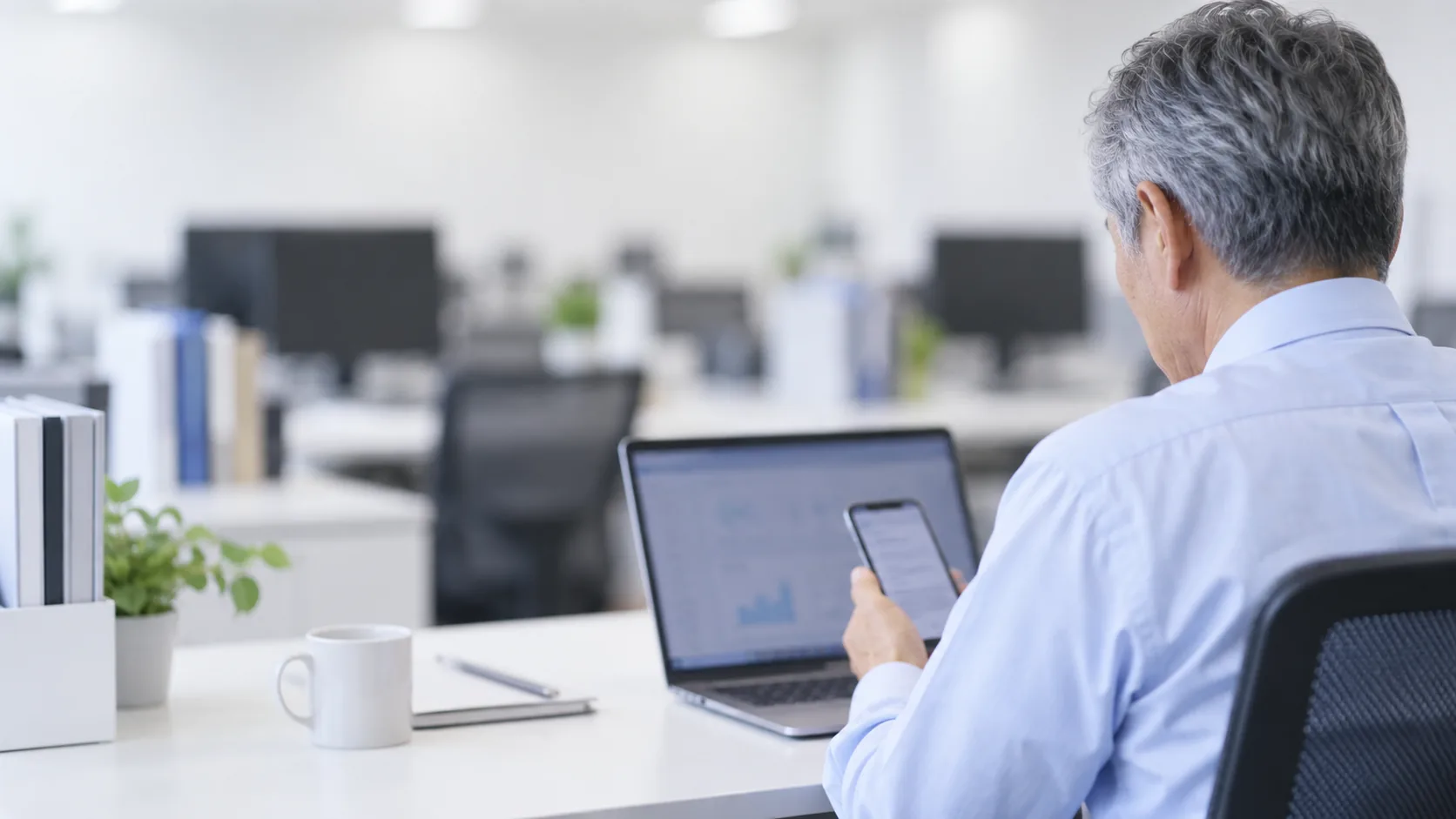 60代前半の日本人男性が自席でのスマートフォン併用をしている場面
