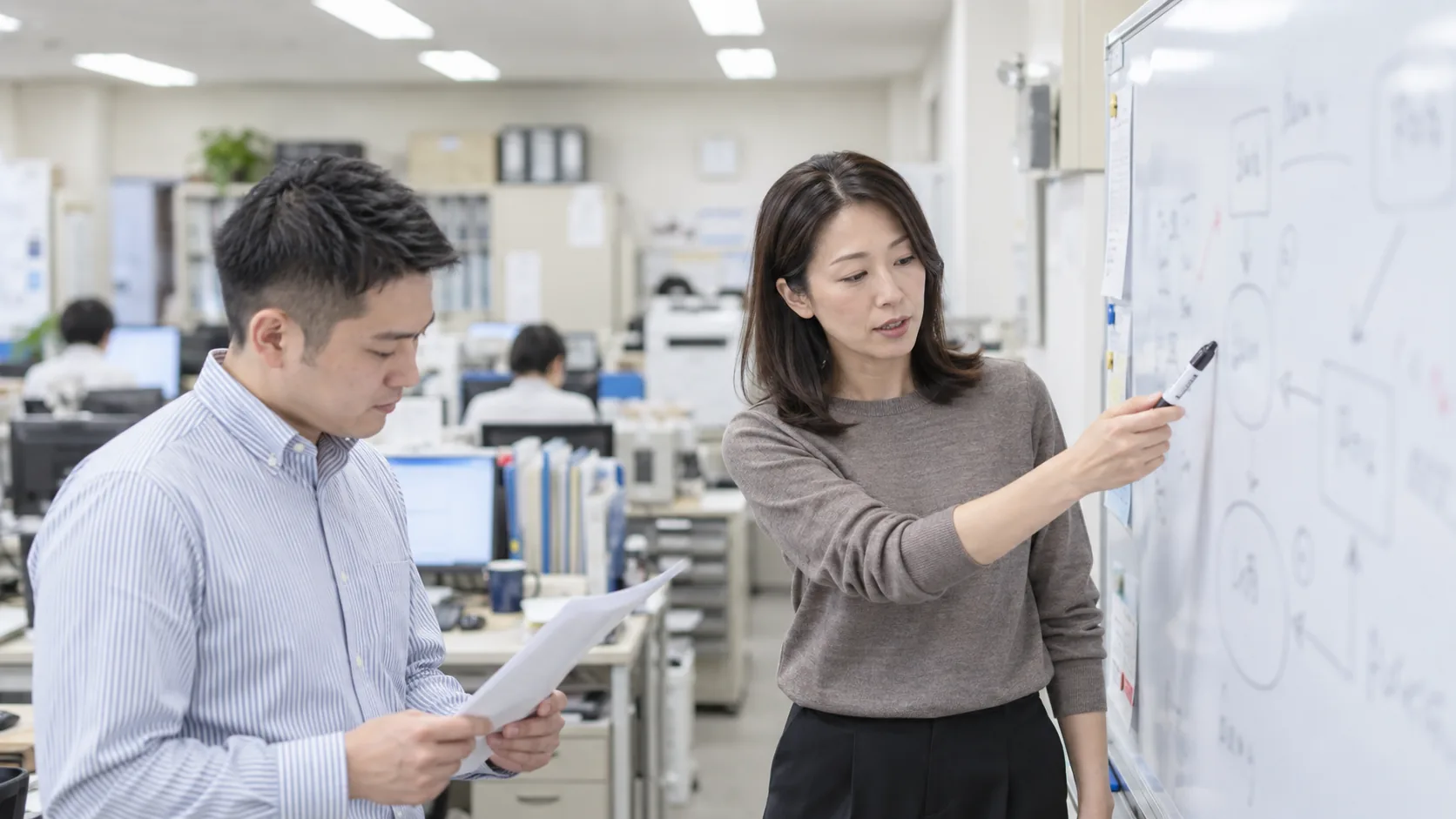 40代前半の日本人女性がホワイトボードでの説明をしている場面